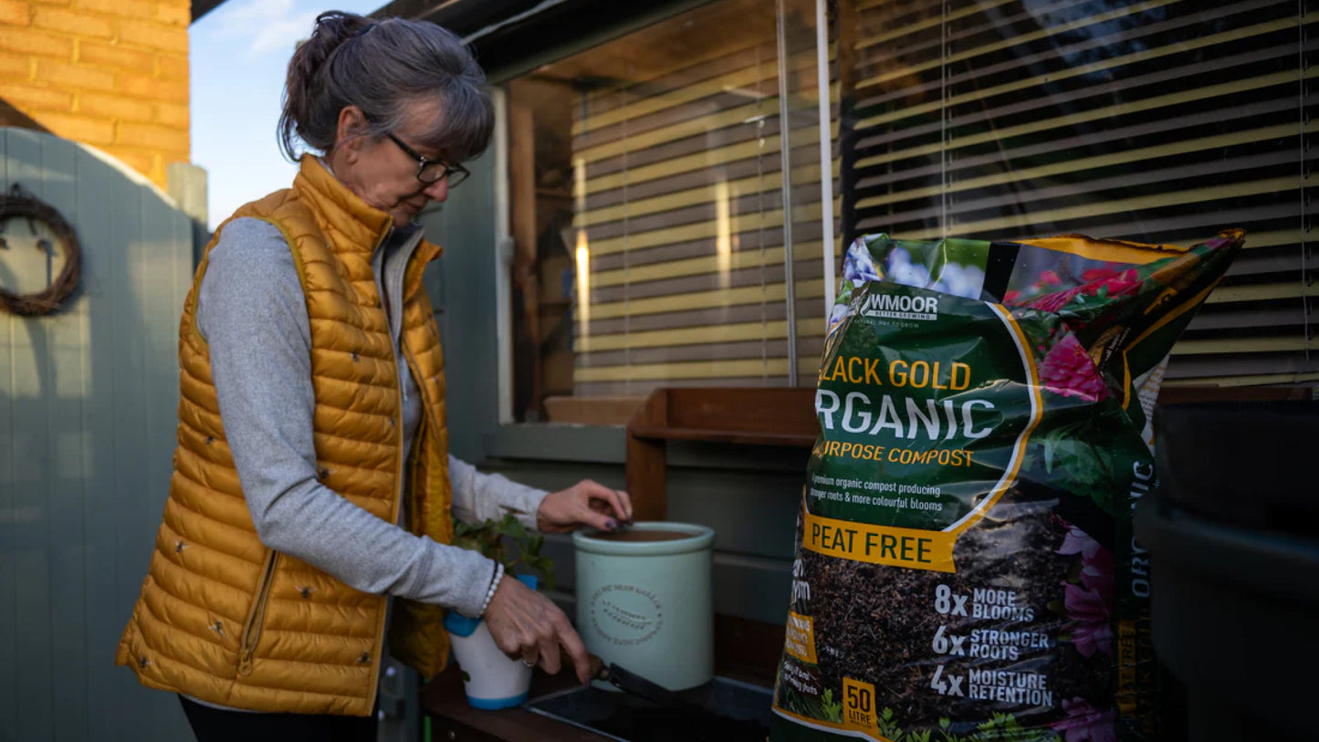 An older lady scoops Growmoor Black Gold Organic compost into a pot with a gardening trowel